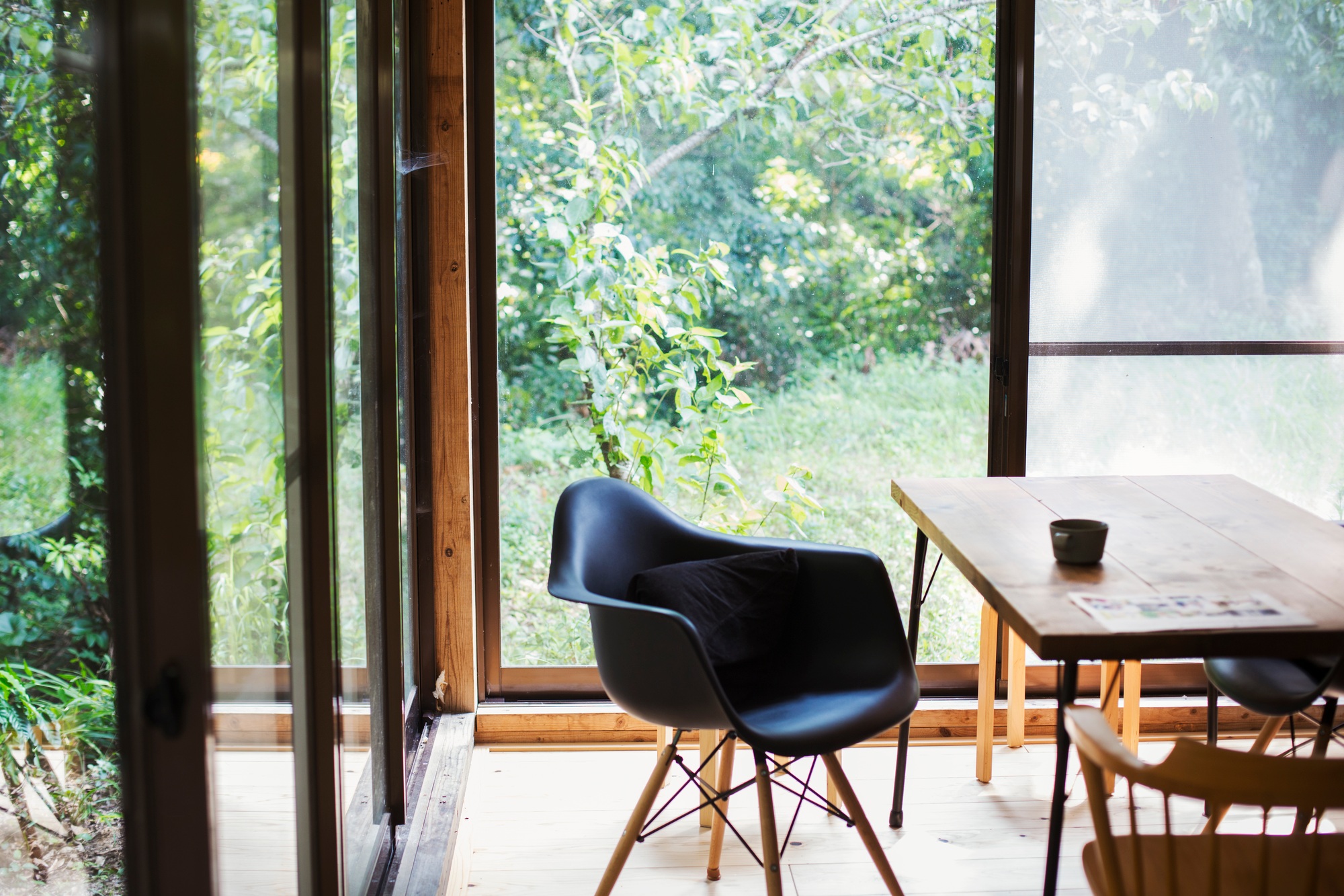 Interior view of residential building with black chair and wooden table, glass walls.
